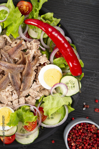Salad with tuna, anchovies and vegetables. Mediterranean food. The background is black. Top view. Copy space. Vertical shot.
