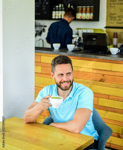 Man bearded guy drinks cappuccino wooden table cafe. Cafe visitor happy smiling face enjoy coffee drink. Improve overall health. Take moment to care about yourself. Coffee drinkers live longer