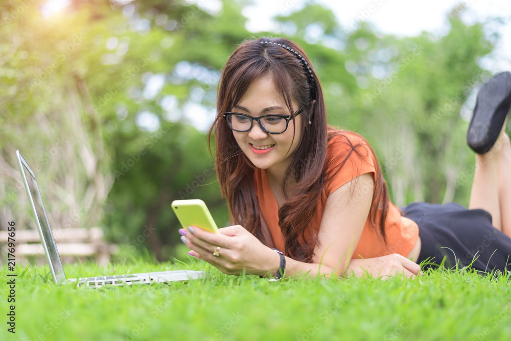 Happy Asian woman using smartphone when relaxing in park. People and lifestyle concept. Technology and Relaxation theme. Outdoors leisure and activity theme. Laptop computer element Happy Asian woman using smartphone when relaxing in park. People and lifestyle concept. Technology and Relaxation theme. Outdoors leisure and activity theme. Laptop computer element
