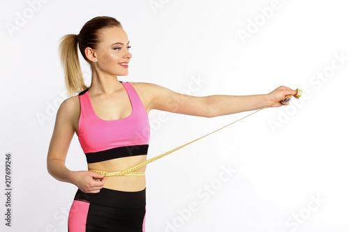 A sporty young girl measures a waist with a centimeter isolated on white background © Alexander
