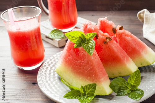 Watermelon sliced on a plate with mint leaves and fresh watermelon smoothie on a wooden background.