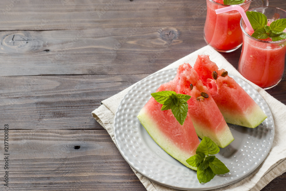 Watermelon sliced on a plate with mint leaves and fresh watermelon smoothie on a wooden background. Copy space