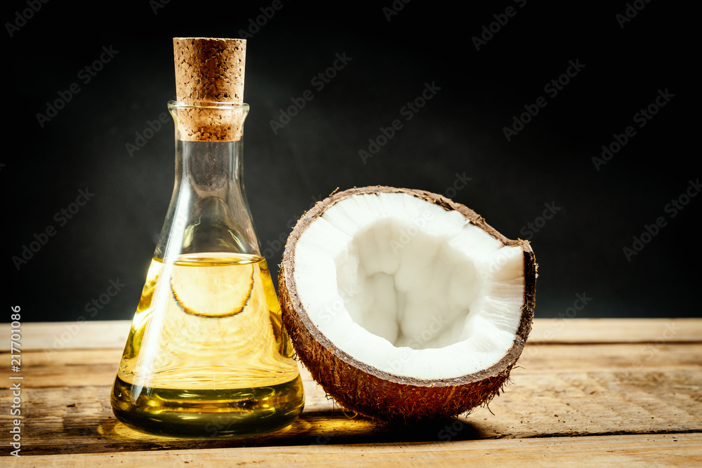 fresh brown coconuts and a bottle of oil on a wooden table on a black background fresh brown coconuts and a bottle of oil on a wooden table on a black background
