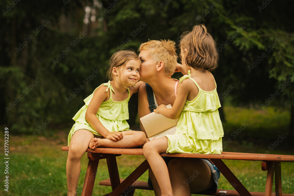 beautiful mother and two adorable daughters in dresses posing on a picnic table in a summer forest beautiful mother and two adorable daughters in dresses posing on a picnic table in a summer forest