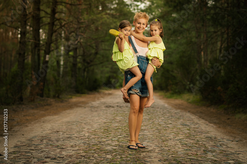 beautiful mother and two adorable daughters in dresses posing on the road in the summer forest