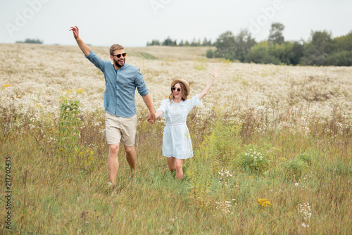 happy lovers holding hands while running in meadow with wild flowers
