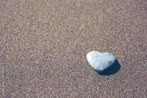 Gray stone in the form of heart lies on sand.