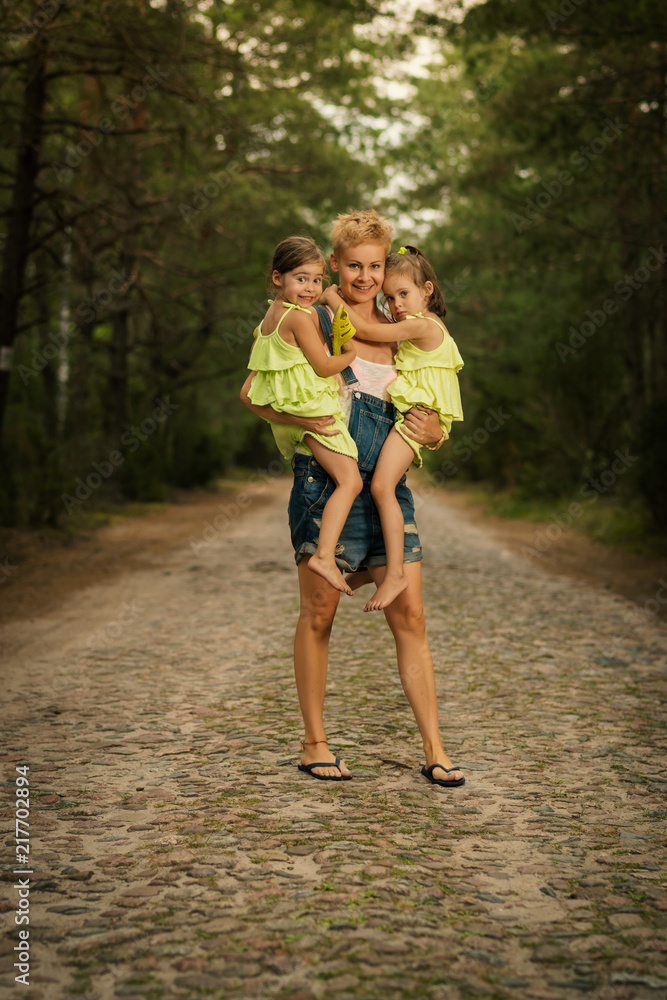 beautiful mother and two adorable daughters in dresses posing on the road in the summer forest beautiful mother and two adorable daughters in dresses posing on the road in the summer forest