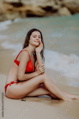 Attractive young woman wearing a red bikini sits on a seabeach