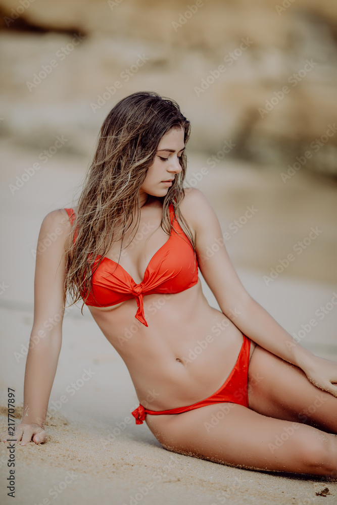 Foto Stock Young beauty Woman with perfect body in red bikini lying on  beach over sea background | Adobe Stock