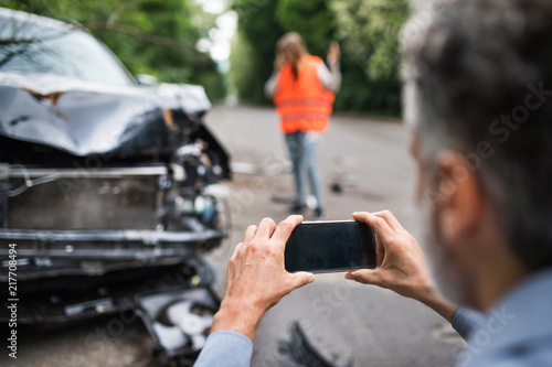 Unrecognizable man taking pictures of a broken car after an accident.