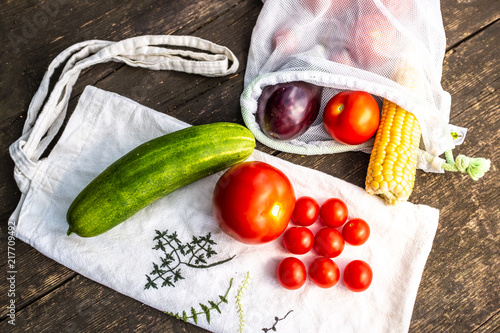 Produce in single use plastic bags and plastic free reusable shopping bags on a wooden surface in nature. Zero waste lifestyle. photo