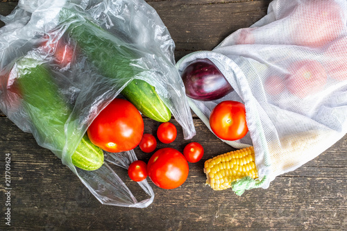 Produce in single use plastic bags and plastic free reusable shopping bags on a wooden surface in nature. Zero waste lifestyle. photo