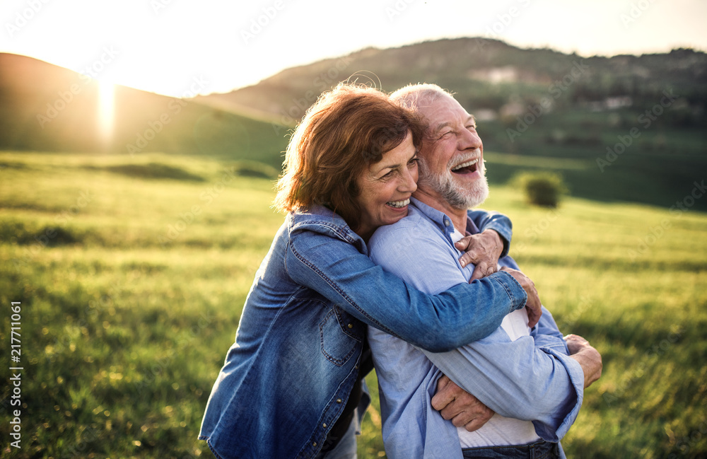 Side view of senior couple hugging outside in spring nature at sunset. - obrazy, fototapety, plakaty 
