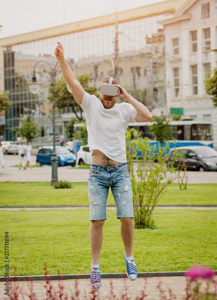 Obraz premium A young man plays a game wearing virtual reality glasses on the street.