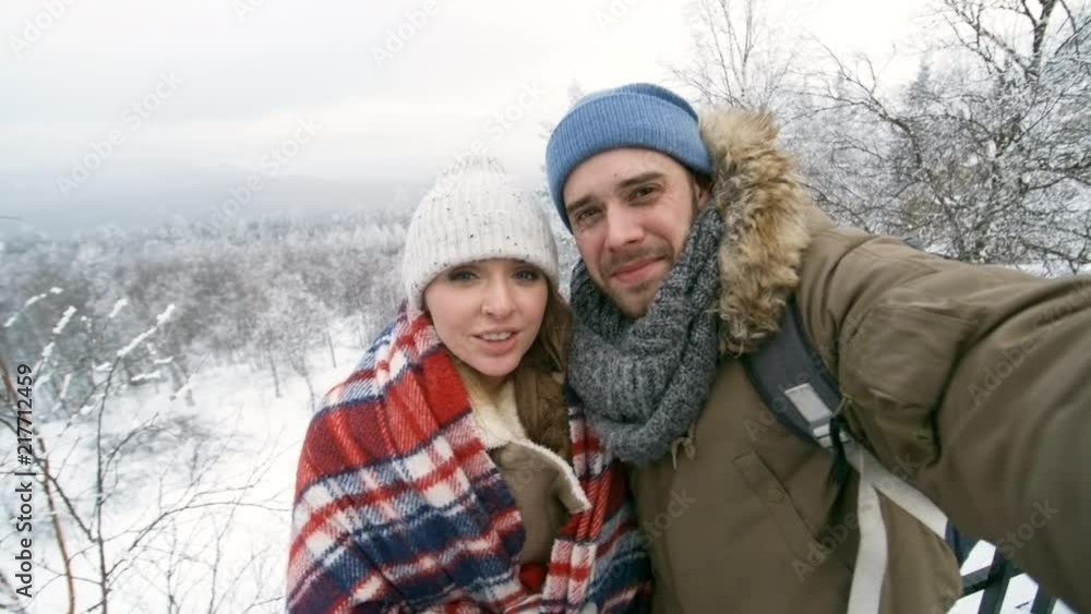 Happy young beautiful woman standing with boyfriend in national park at winter day, pointing at mountain and telling about something at camera while recording video for travel blog Happy young beautiful woman standing with boyfriend in national park at winter day, pointing at mountain and telling about something at camera while recording video for travel blog