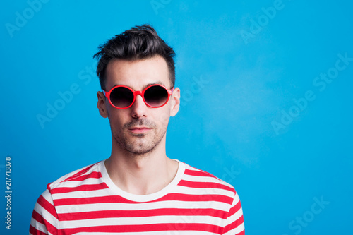 Portrait of a young man in a studio with sunglasses on a blue background.