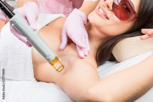 Laser cosmetology Armpit hair removal. Beautiful smiling woman client in red glasses having procedure. Professional skin beauty care
