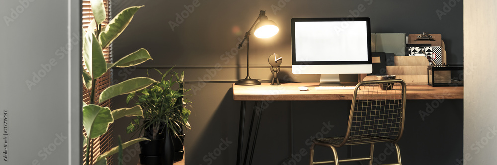 Creative golden, metal chair by a wooden desk with computer screen, folders and an industrial luminous lamp in a stylish home office interior Creative golden, metal chair by a wooden desk with computer screen, folders and an industrial luminous lamp in a stylish home office interior