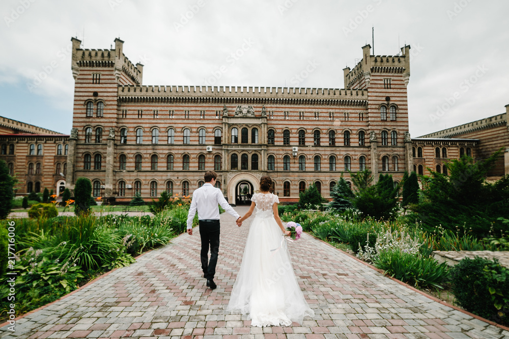 Newlyweds go back to the ancient restored architecture, old building, old house outside, vintage palace outdoor.