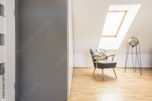 Patterned armchair next to modern lamp on wooden floor on attic interior with window. Real photo