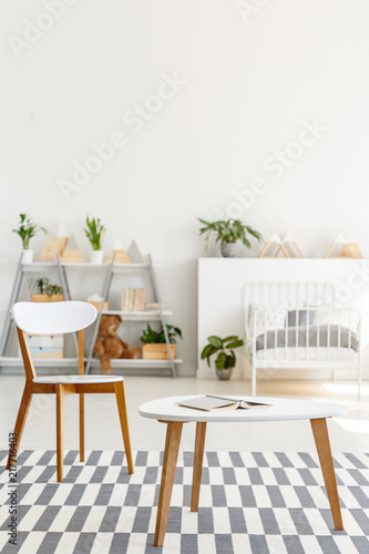 Table and chair on patterned carpet in white kid's bedroom interior with plants. Real photo