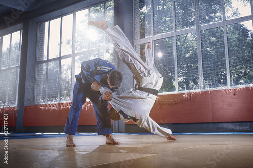 Fototapeta Dwóch wojowników judo wykazujących się umiejętnościami technicznymi podczas uprawiania sztuk walki w klubie walki. Dwaj przystojni mężczyźni w mundurach. walka, karate, trening, sztuka, sportowiec, koncepcja konkurencji