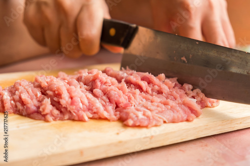 Chef is chopping the raw pork on the wooden cutting board with a sharp knife to cook in the kitchen.
