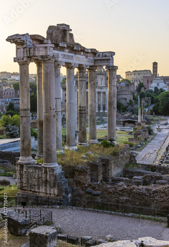 Roman ruins lit by early morning light. There is Colosseum in the background