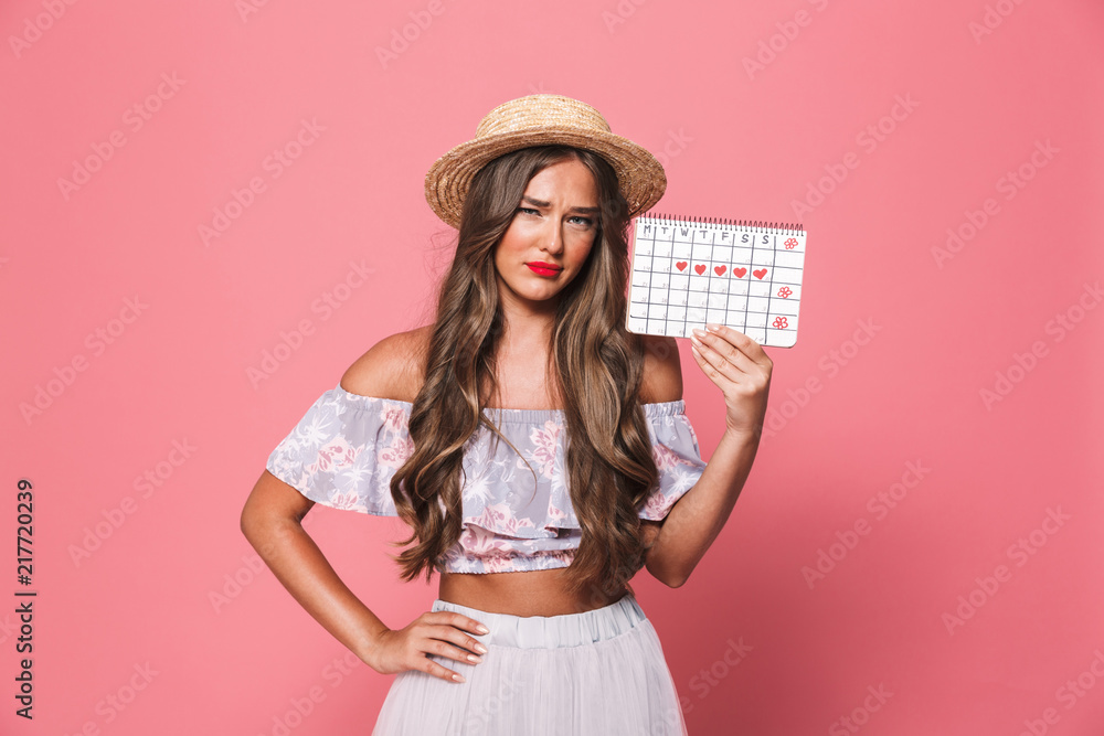 Portrait of caucasian woman 20s wearing straw hat holding period calendar, isolated over pink background in studio Portrait of caucasian woman 20s wearing straw hat holding period calendar, isolated over pink background in studio
