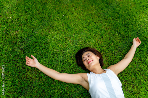 Asian woman laying down and spreading arms on grass field