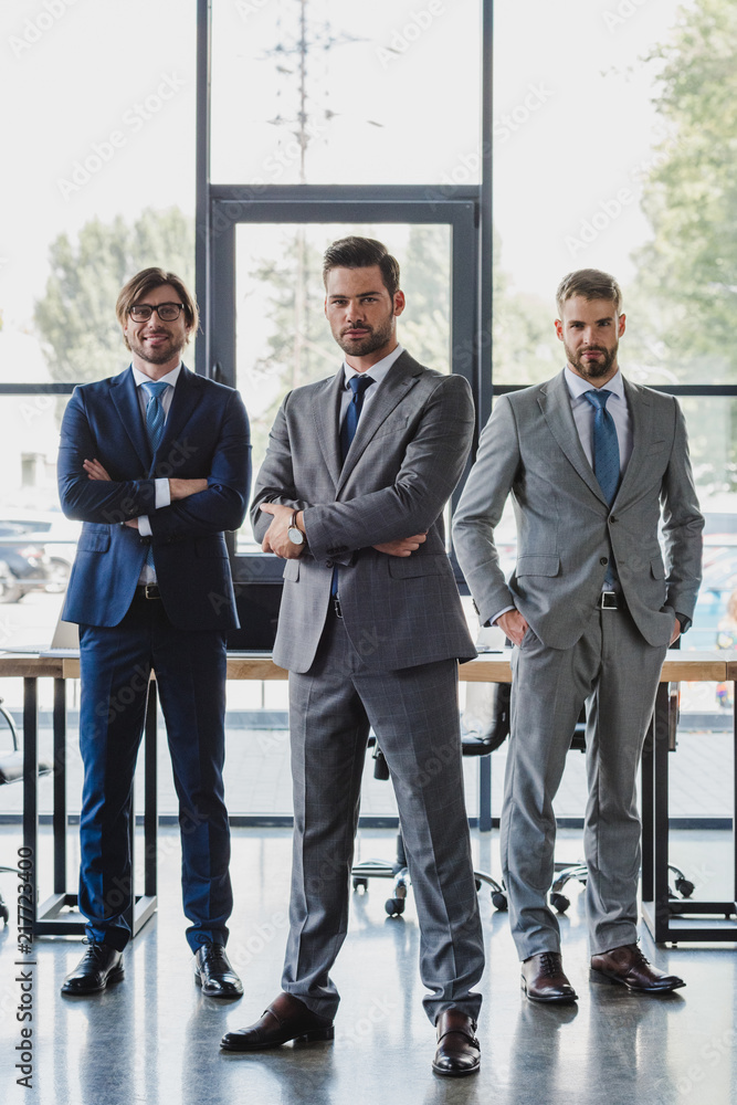 Fototapeta premium confident young businessmen in formal wear standing together and looking at camera in office
