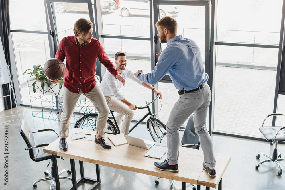 high angle view of young businessmen having fun with basketball ball in office