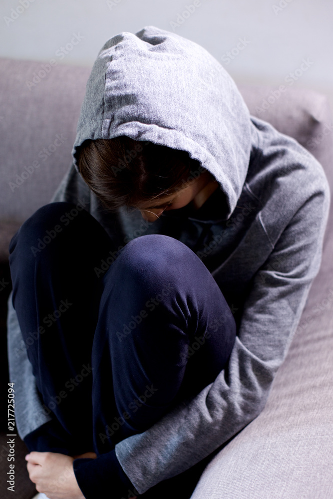 Sad young woman with hood thinking feeling lost sitting on sofa medium shot Sad young woman with hood thinking feeling lost sitting on sofa medium shot