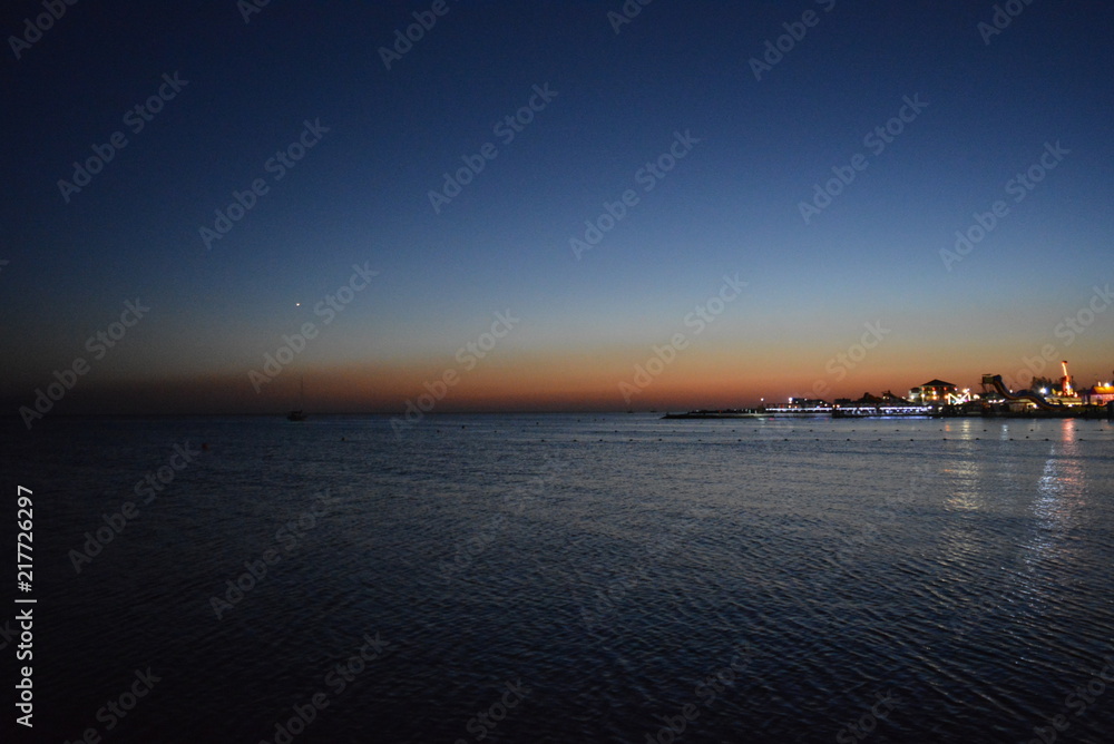 Beautiful sea water with reflection and the embankment of the Black Sea, houses with bright lanterns at sunset at sunset