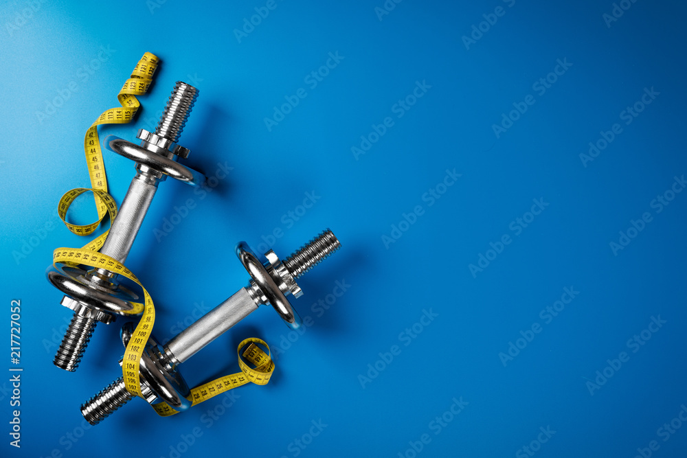 dumbbells and measuring tape on blue background with copy space