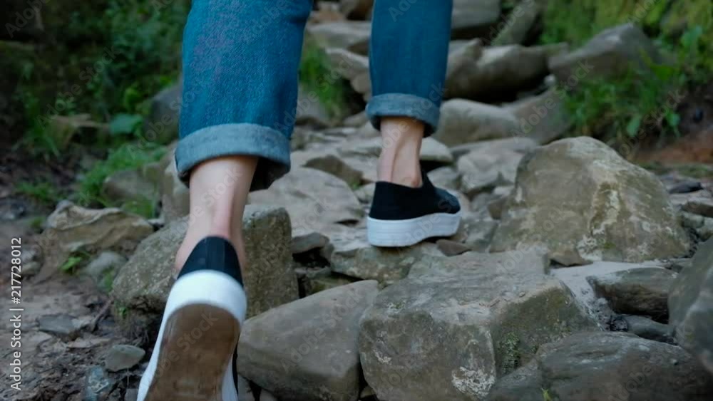 legs of a woman in jeans and crossover, walking alone on a mountain path with a lot of stones legs of a woman in jeans and crossover, walking alone on a mountain path with a lot of stones