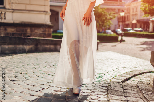 Beautiful woman wearing white wedding dress outdoors in summer. Lady walking by palace at sunset