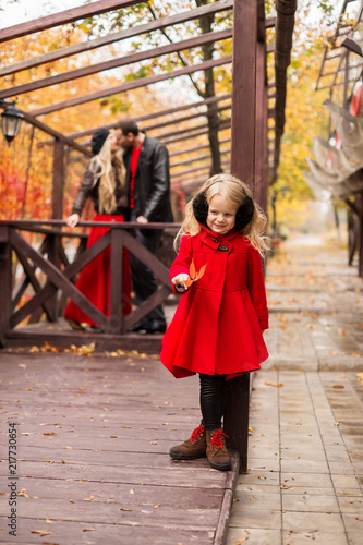 a girl with blond hair plays a leaf at a wooden pillar from behind on a blurred background her parents