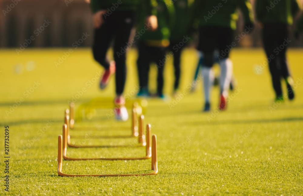 Kid Young Athletes Training with Football Equipment. Football Speed Training. Young Footballer in Blue Sportswear at Training Session on Grass Soccer Field Kid Young Athletes Training with Football Equipment. Football Speed Training. Young Footballer in Blue Sportswear at Training Session on Grass Soccer Field