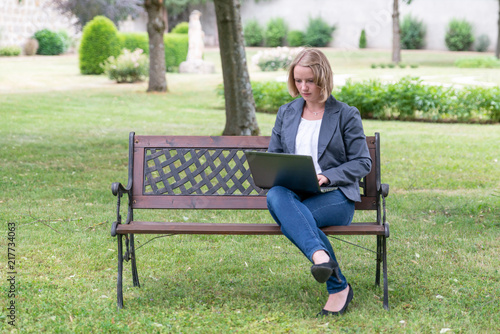 junge hübsche Frau sitzt im Park und schreibt am Laptop, virtual, Homeoffice, Videokonferenz, WLAN, 5G