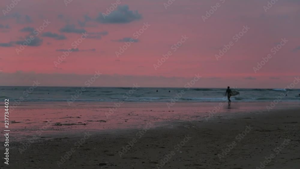 Surfer walking on the beach with pink sky sunset Surfer walking on the beach with pink sky sunset