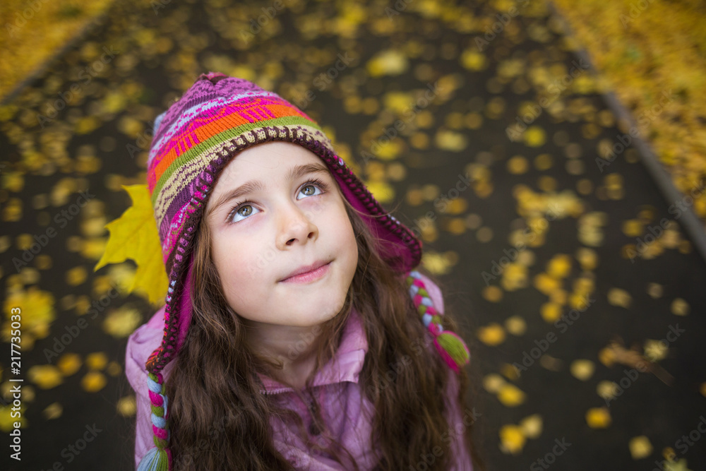 girl in autumn clothes and funny hat on the background of yellow leaves looking up to the right. school child looks at leaf fall girl in autumn clothes and funny hat on the background of yellow leaves looking up to the right. school child looks at leaf fall
