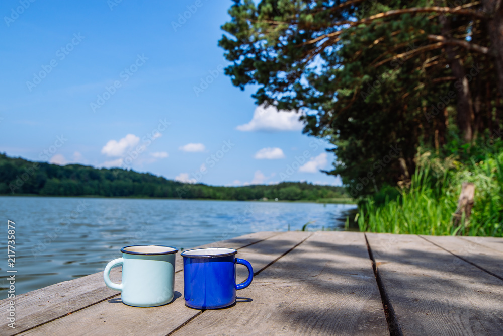 Naklejka premium two metal cups with tea. river on background. summer time concept