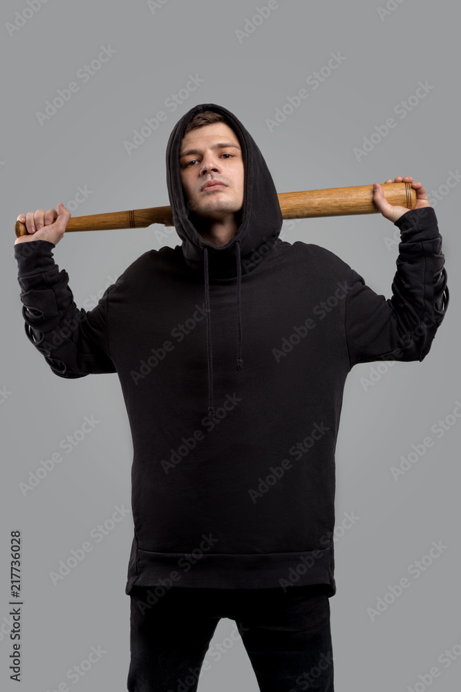 A young guy dressed in a black sweatshirt with baseball bat on grey background in studio Stock Photo Adobe Stock