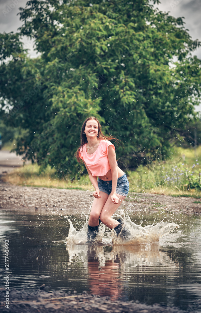 Fototapeta premium happy girl jumping in a puddle in the rain