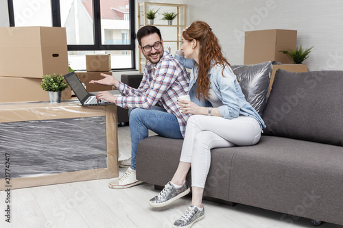 Young couple in new home with notebook sitting on sofa and planning with unpacked boxes in background