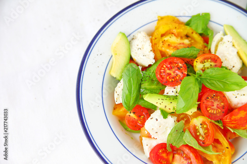 Overhead of fresh salad with cherry and heirloom tomatoes, avocado, burrata cheese, basil and black pepper