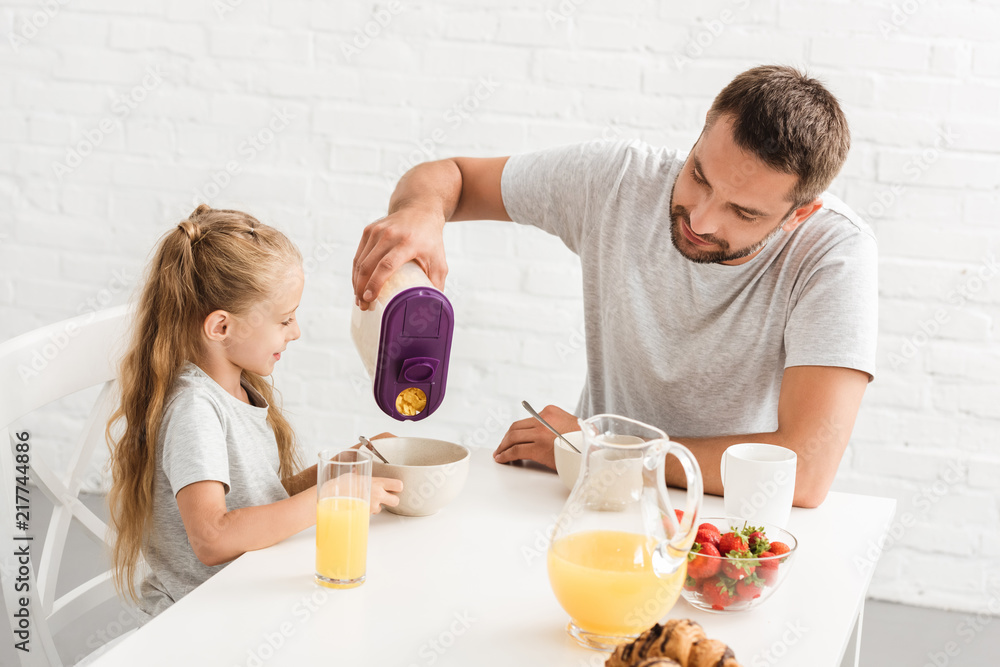 father and daughter eating cornflakes at kitchen father and daughter eating cornflakes at kitchen