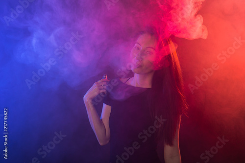 Portrait of asian woman smoking vape or e-cigarette in neon light at black background. © satura_